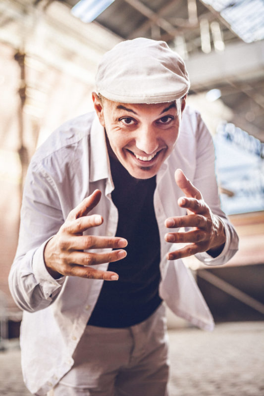 Photo du chanteur HK penché en avant mains ouvertes avec un grand sourire